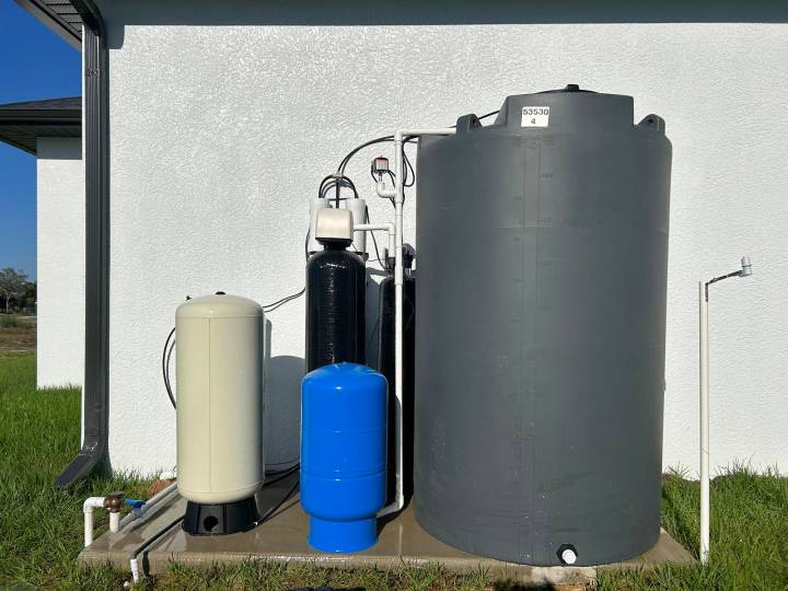 Gray storage tank with filter and pressure tanks against a white wall
